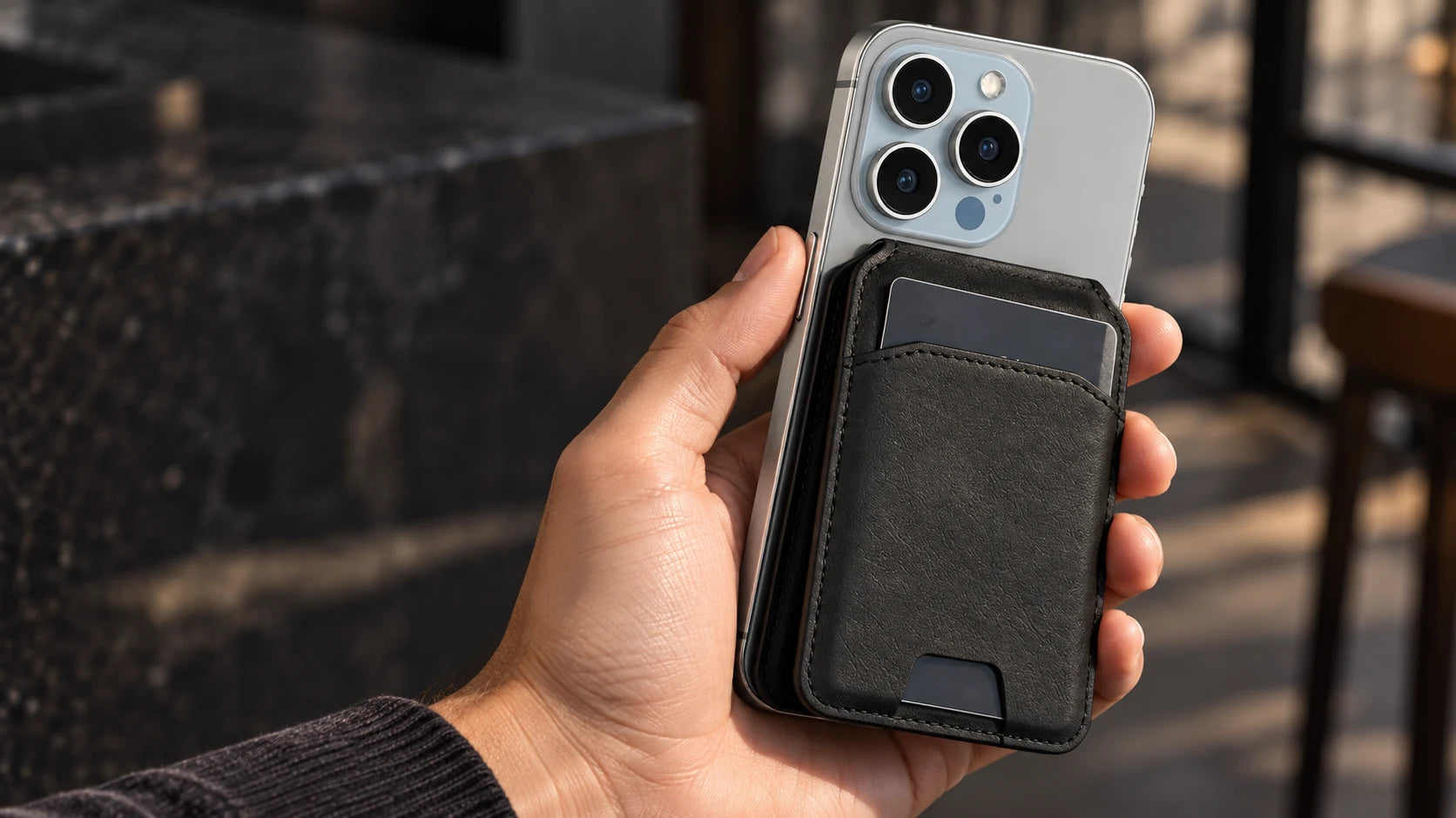 A hand holding a silver phone with the black MagSafe Bifold attached